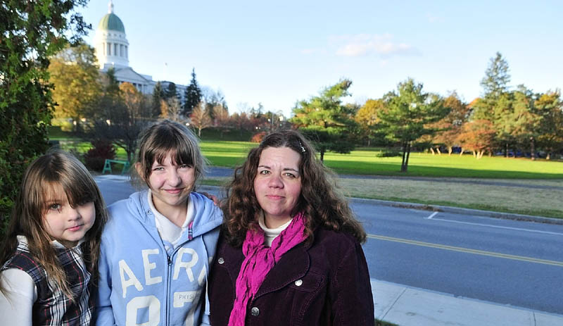 TOO CLOSE TO CAMPSITE: From left, Beth, Olivia and Marcie Rheaume stand on the front porch of their Augusta home next to Capitol Park and the Occupy Augusta campsite, which is behind the trees on right. The Rheaumes are no strangers to protests or other public events next door to their 118-year-old Union Street home — especially since Occupy Augusta began.