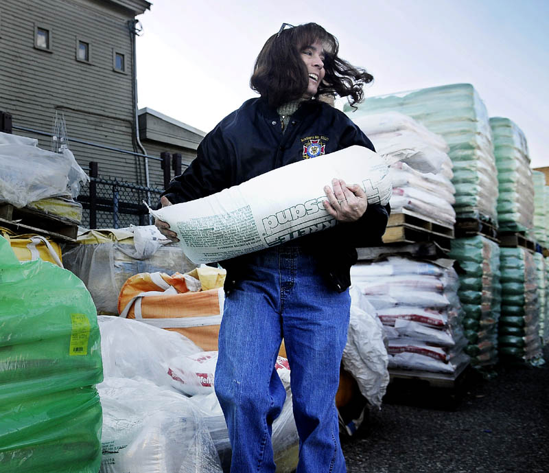 HERE IT COMES: Syrena Touchton loads a tube of sand Tuesday into the bed of her pickup at Harvey’s Hardware in Gardiner. The load adds ballast for the truck to operate in the snow, Touchton said. Hardware stores across Maine had a flood of customers buying shovels, salt and sand.