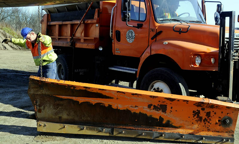 GETTING READY: Augusta Public Works employees Mark White, right in cab, and Don McKinzie guide a plow onto a plow truck Tuesday at the city’s garage. State and municipal crews were preparing their rigs for snowfall that has been forecast for today.