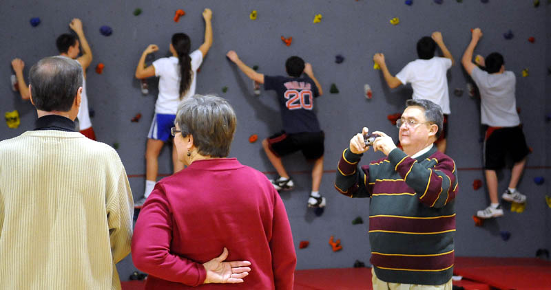 Cony High School Class of 1961 member Ron Roussel, right, takes a photo Tuesday of classmates David Dun and Sharon Mertzel while Cony students climb the new wall purchased by the alumni. The class of ’61 raised $4,200 to help purchase the horizontal wall for students at the Augusta school while planning their 50th class reunion last year. Class of 1961 member Connie Hanson said the class is challenging other Cony alumni, as they hold their own class reunions, to follow suit and also give back to Cony.