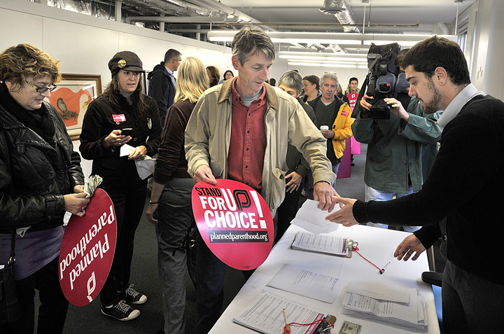 Mark McCain, center, of Portland, was one of many who donated cash to Planned Parenthood in Portland Friday morning. Planned Parenthood staff member Eric Covey, right, thanks them for their contributions and support.