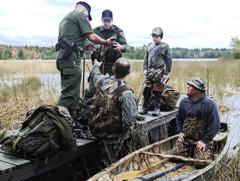 CHECK UP: Game Wardens Terry Hughes, left, and Dave Simmons inspect a mixed bag of ducks Monday collected by hunters Paul Downs, bottom second from left, Jim Deaton, right, and Downs' 10-year-old son, Camryn, on Lake Cobbossee in West Gardiner. State and federal wardens were checking migratory bird hunters on the first morning of duck season in the southern zone of Maine, which is also the opening day of bird season across the state. "We had a lot of misses," Deaton said despite bagging several ducks. "But it's still a good day." The men were not issued any summonses.