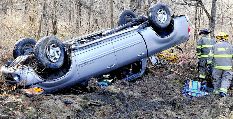 Sidney firefighters survey a Toyota truck that rolled over on a shaded portion of West River Road, near the Dinsmore Road, on Sunday. State police Trooper Rick Moody said the accident was caused by slippery road conditions and the female operator complained of neck pain. A snowmobile in back of truck was ejected and also damaged.