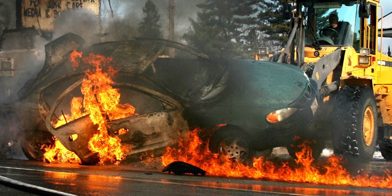 A 2000 Pontiac Grand Am burns on Norridgewock Road in Fairfield Tuesday. A nearby business owner, Bill Lybrook, tipped the car with a front-end loader to allow firefighters access to the undercarriage.