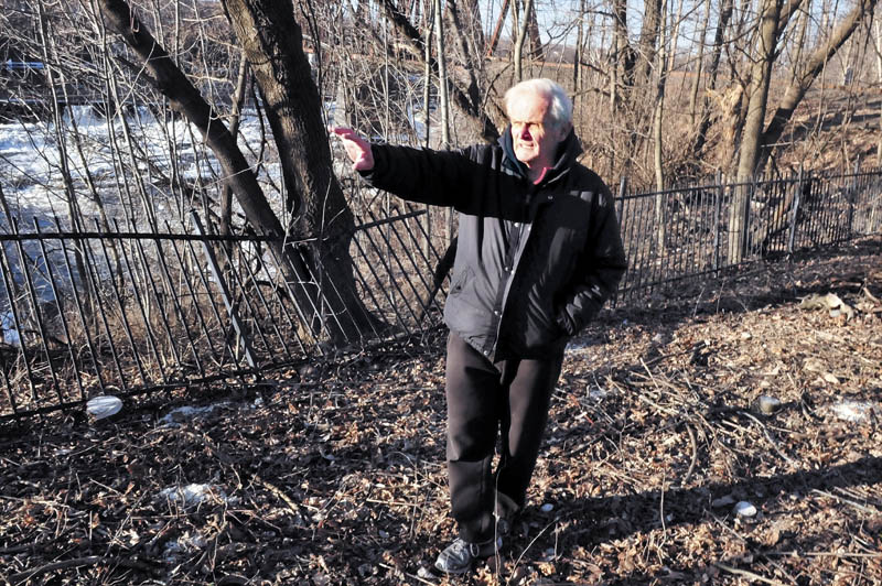 Jack Nivison speaks from a wooded area beside the Kennebec River, on the Winslow side of the Ticonic Bridge, where crews have cleared debris on Tuesday. The site is near where a barber shop, drug store and photography shop once stood.