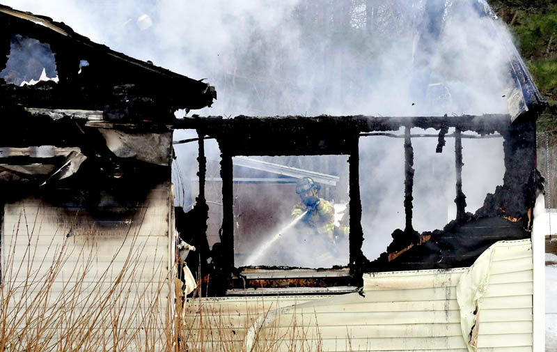 A firefighter can be seen through burned-out windows and walls while fighting a fire that destroyed a mobile home in Sidney on Tuesday.