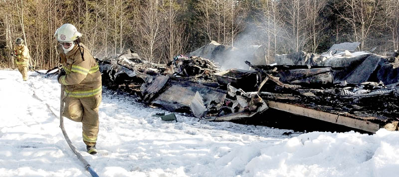 Troy Fire Chief Larry Raymond, front, and firefighter Jerret Roy haul hoses past a smoldering mobile home, off U.S. Route 202, that was destroyed on Saturday. Raymond said the mobile home, owned by Margaret Henderson, was reported on fire at 2:30 p.m. He said the structure was used to store personal items, clothes and household goods. The State Fire Marshal's Office has been called to determnine a cause. There were no injuries. It was the second major fire in a week in Troy.