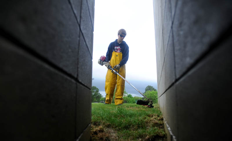 Cameron Mills, 21, of the Colby College grounds crew, whacks weeds in his rain slickers as rain falls in Waterville Friday afternoon.