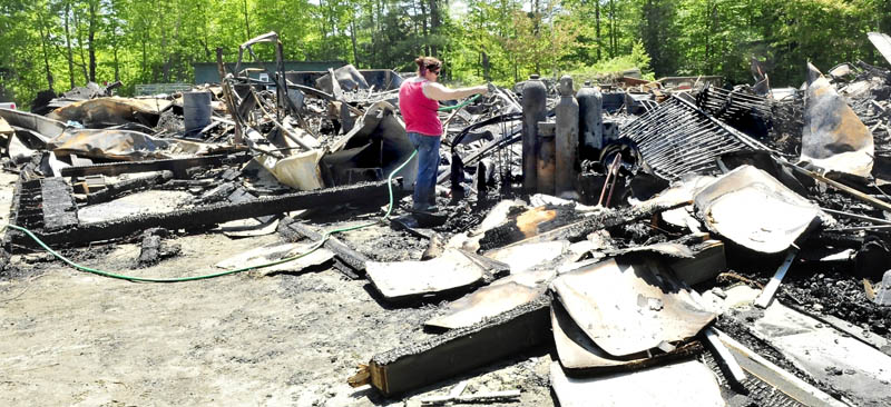 Camp Mataoka employee Michelle Oliver on Tuesday sprays water on the smoldering remains of a two-story maintenance building that was destroyed by fire in Smithfield Monday evening. Camp owner Jason Silberman said that a cause has not been determined. He said the insured building was full of tools and equipment and no one was hurt. Silberman added the building will be rebuilt and would have no impact on this years camp season, which begins June 23.