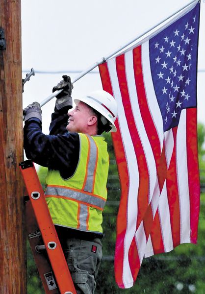 Tom Williams of the Fairfield Public Works department places an American flag in town on a rainy Tuesday.