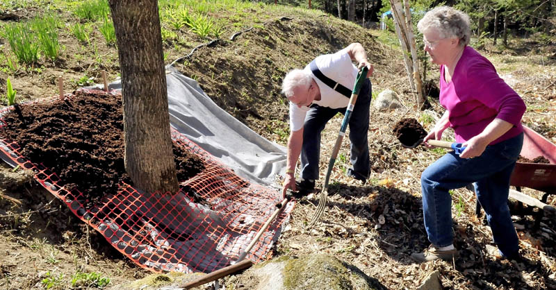 Wilmer and Marlene Redlevske shovel mulch over a tarp to keep weeds from encroaching on a flower garden at their home in Mercer recently.