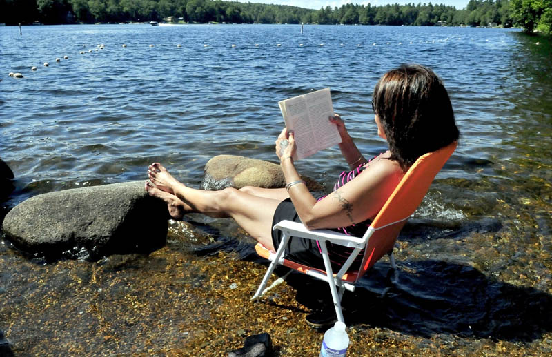 Laurie Bushey soaks her feet in Messalonskee Lake in Oakland while reading a book on a warm Thursday.