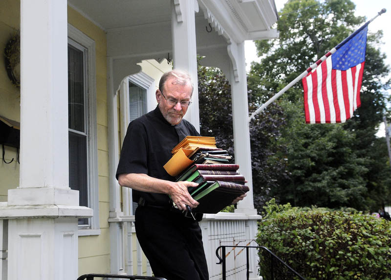 The Rev. Father Frank Morin carries the sacramental registers from the rectory of Sacred Heart Catholic Church in Hallowell on Sept. 5,'The priest at Sacred Heart, George Hickey, recently passed away, leaving the church without a pastor. The paper records of baptisms, first communions, confirmations, marriages and deaths were relocated to St. Michael Catholic Parish to be stored with other church documents.