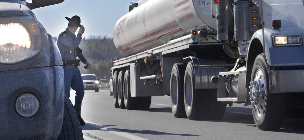 CLOSE CALL: Maine State Trooper Chris Rogers holds on to his Stetson Thursday as a tractor-trailer passes him during a traffic stop in West Gardiner. Several State Police cruisers have been struck while parked at accidents this year, compelling police to remind drivers that they must slow down and pull over when approaching emergency vehicles.