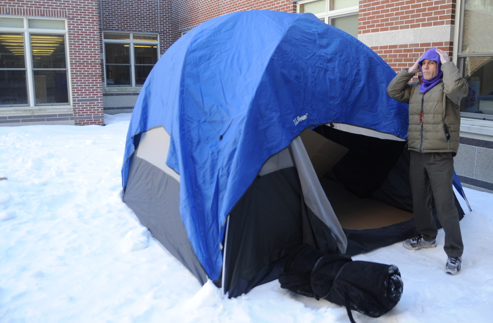 OUT IN THE COLD: Cony High School English department chairman Tom Wells covers up his head Thursday while preparing a tent at the school to sleep in over night. Four Cony High School teachers were chosen by students to spend the night outside at the school as part of a fundraiser for the Augusta warming center.