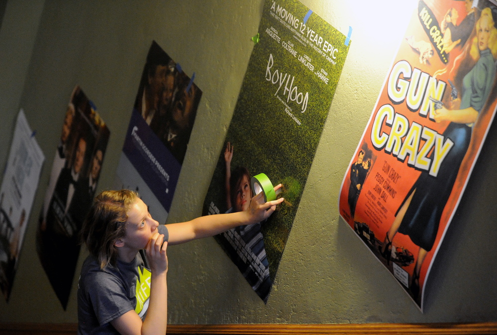 Bria Watson, MIFF venue manager, hangs posters in the lobby of the Waterville Opera House in Waterville on Thursday. The Maine International Film Festival kicks off this weekend.