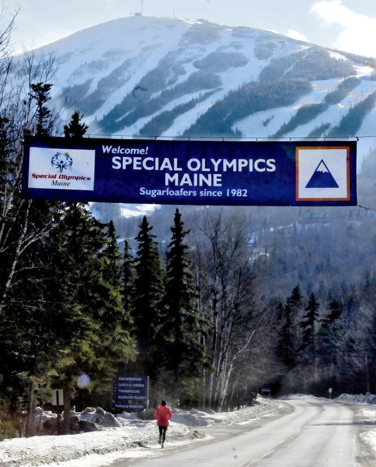 As man-made snow blows on Sugarloaf mountain, a runner heads up the access road on Sunday under a banner for the Special Olympics Maine Winter Games. Tuesday events have been canceled because of the snowstorm.