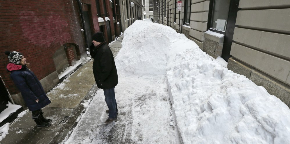 Two office workers take a break on Hawes Street, which is unplowed and covered in about 5 feet of snow, in the Financial District of Boston on Tuesday.