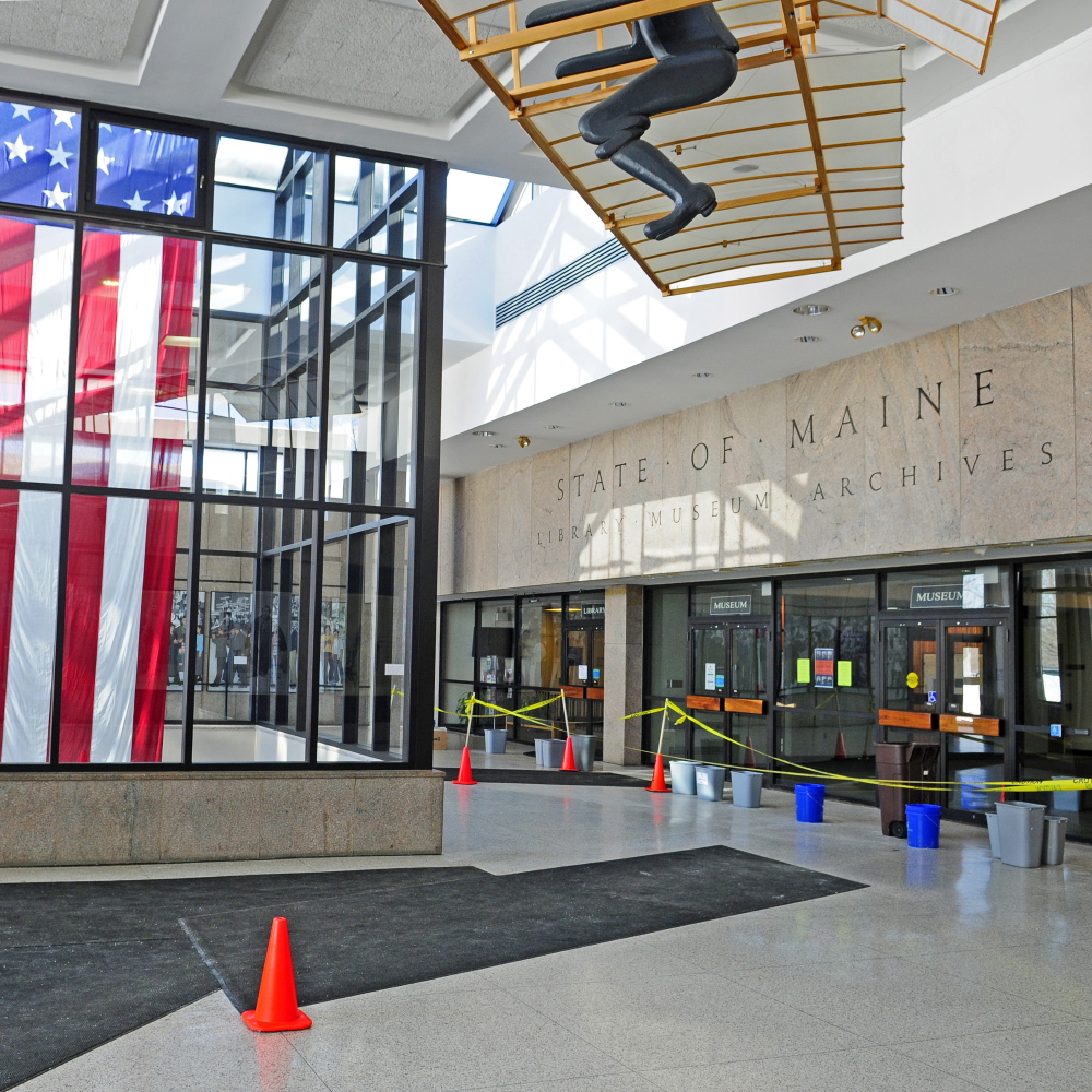 In front of the doors to the state’s library, museum and archives, buckets and trash cans catch drips from the leaky ceiling Wednesday in the Maine State Cultural Building’s lobby in Augusta.