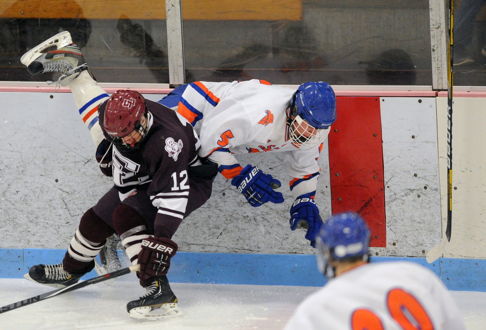 Staff photo Michael G. Seamans 
 Lawrence/Skowhegan's Adam Littlefield (5) gets checked into the boards by Edward Little's Matt Verrill (12) during an Eastern A quarterfinal Tuesday night at Sukee Arena.