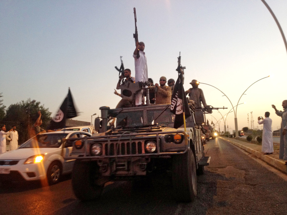 In this photo taken Monday, June 23, 2014, fighters from the Islamic State group parade in a commandeered Iraqi security forces armored vehicle down a main road at the northern city of Mosul, Iraq.