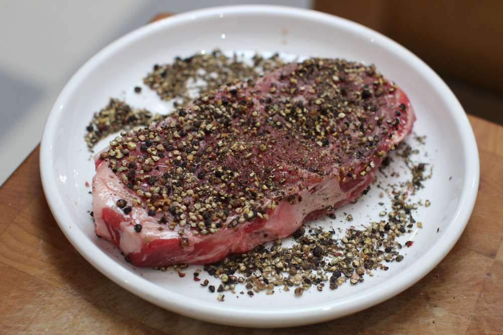 Coating the steak with black pepper.