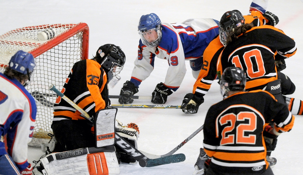 Messalonskee High School’s Jared Cunningham (19) dives over Winslow High School defender Jacob Larsen (12) as Winslow goalie Andrew Beals (35) makes the save in the second period in the Eastern Class B championship last week at Alfond Arena at the University of Maine.