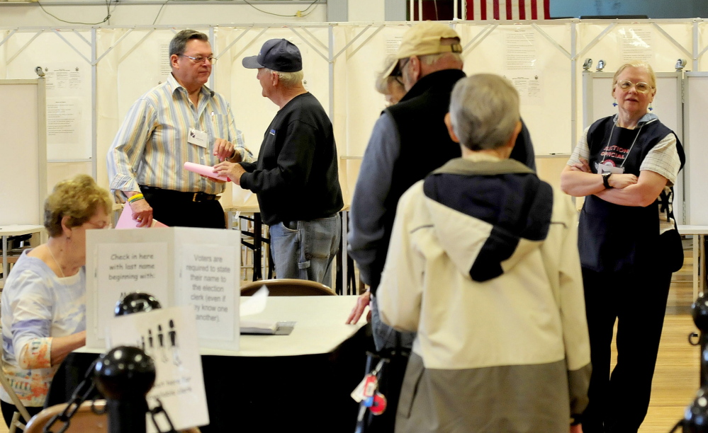 Election Warden Herb Oliver, left, hands ballots to residents during elections on the city trash issue in Waterville on Tuesday.