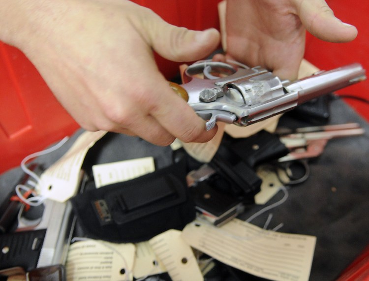 Augusta police Officer Brad Chase examines a pistol before recovering records about the gun in storage Wednesday at the police station.