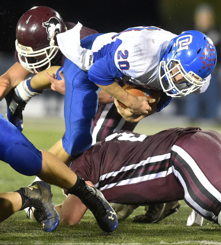 Oak Hill’s Levi Buteau (20) dives over Maine Central Institute’s Alex Bertrand (2) during the Class D state championship game Friday night at Alfond Stadium in Orono.