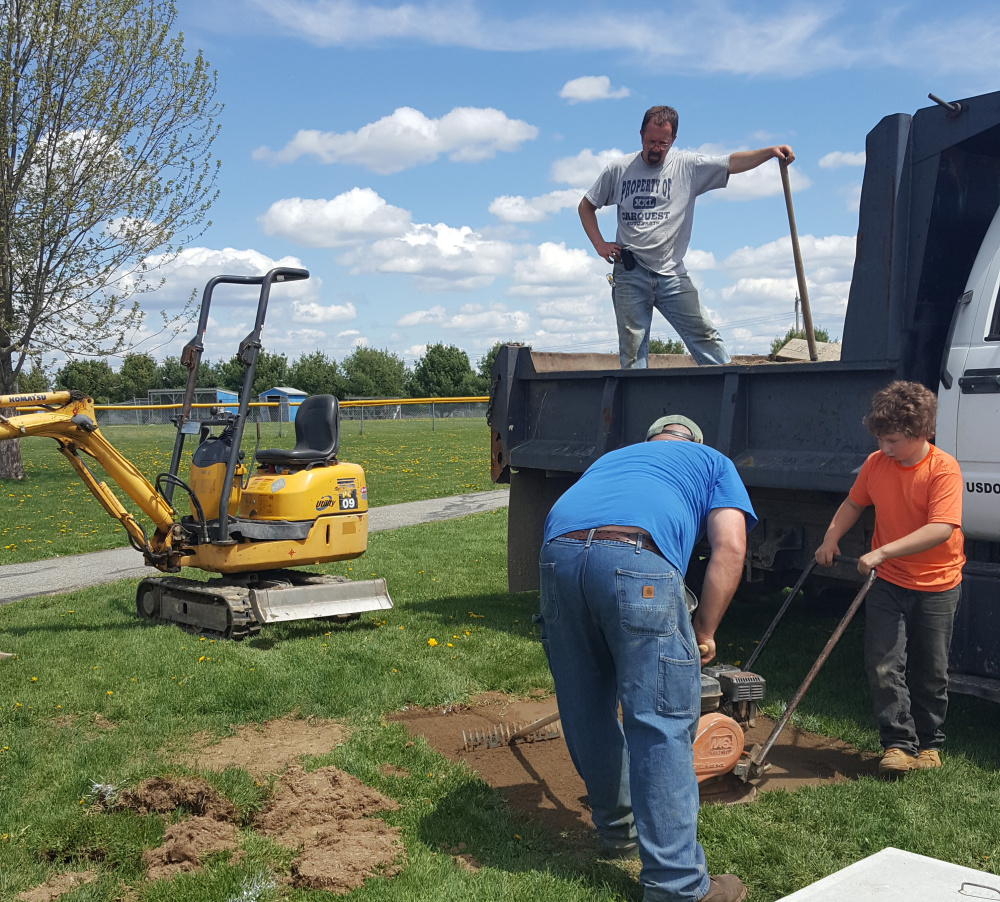 Volunteers Greg Parker, in truck, Liam Poulin and Jason Dumais, back to the camera, help install buddy benches at Benton Elementary School. Liam's father, Len Poulin, who owns a construction and excavation business, volunteered to install the benches, bought with money raised by the Student Council.