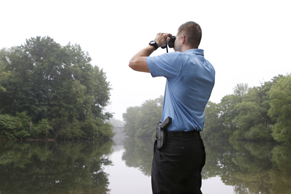 Police officer Garrett McCarthy scans the Presumpscot River's banks in Westbrook on Wednesday, looking for a non-native species of snake believed to be lying dormant after eating a beaver.