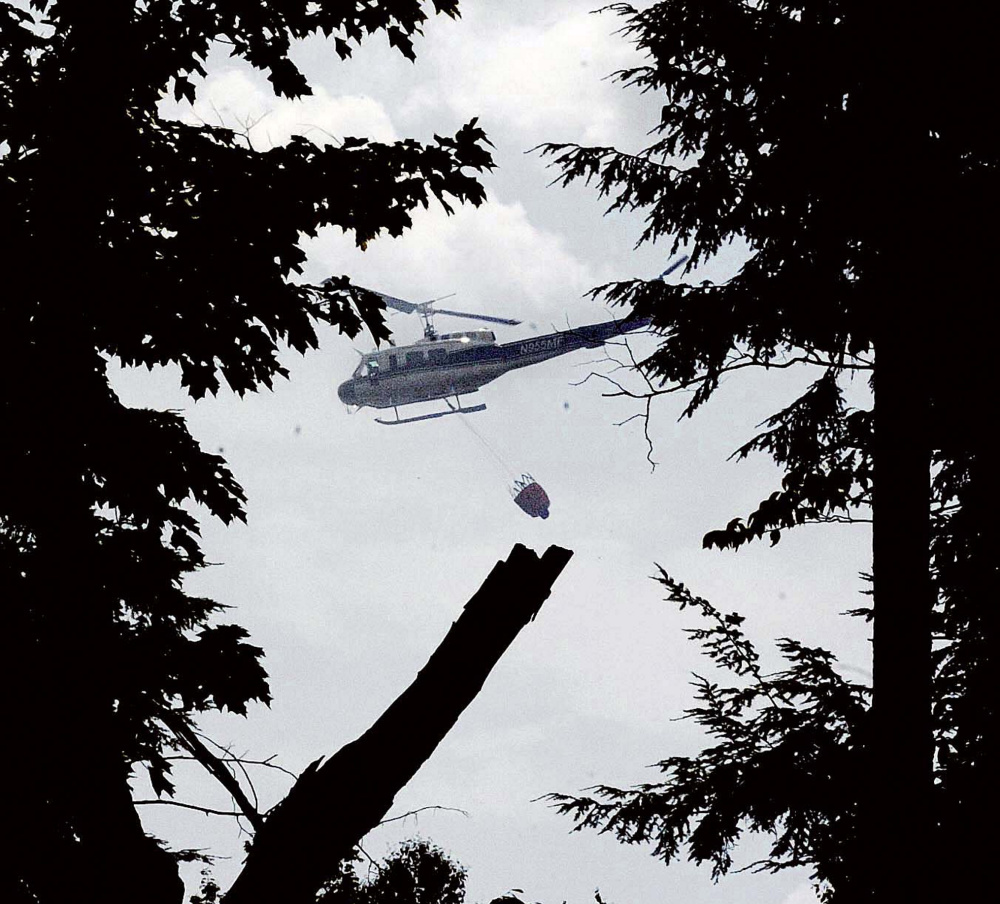 A Maine Forest Service helicopter dumps water over a woods fire Tuesday off Gray Road in Vassalboro. The fire, which was in a hard-to-reach area, burned until Wednesday morning.