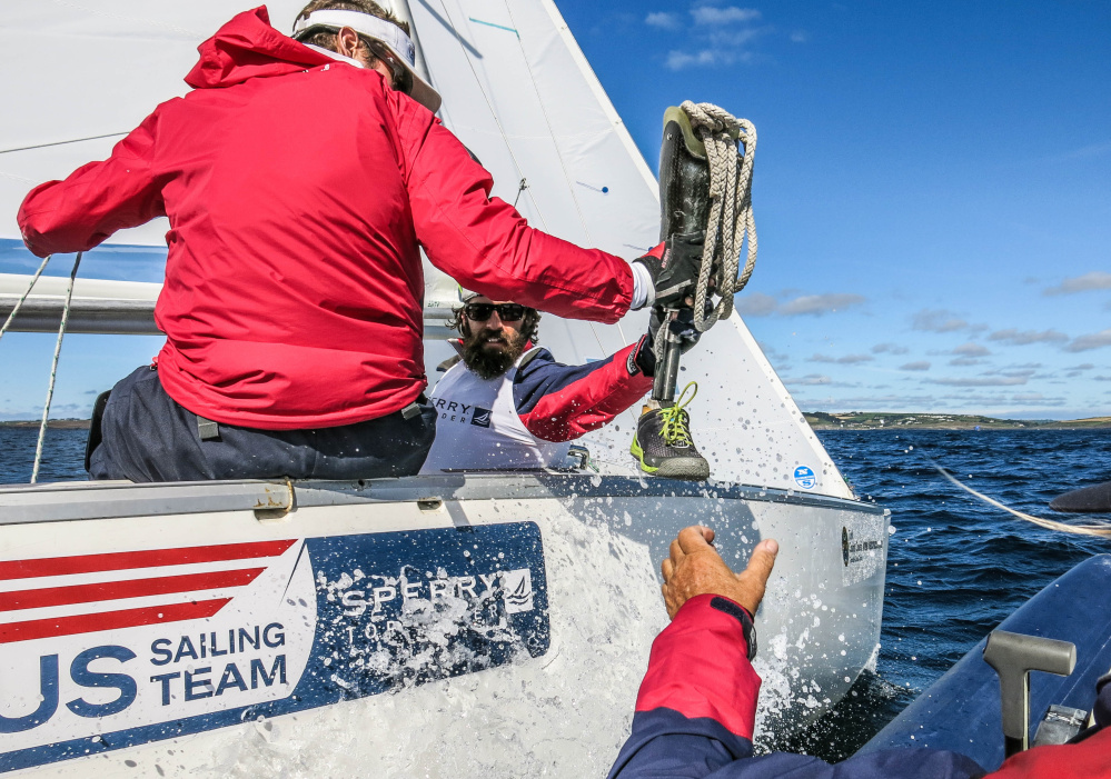 Hugh Freund removes his prosthetic lower leg and hands it to a coach. The prosthesis is not allowed during Paralympic competition. Each of the three sailors in the Sonar class is assessed a point value, depending on the severity of their disabilities.