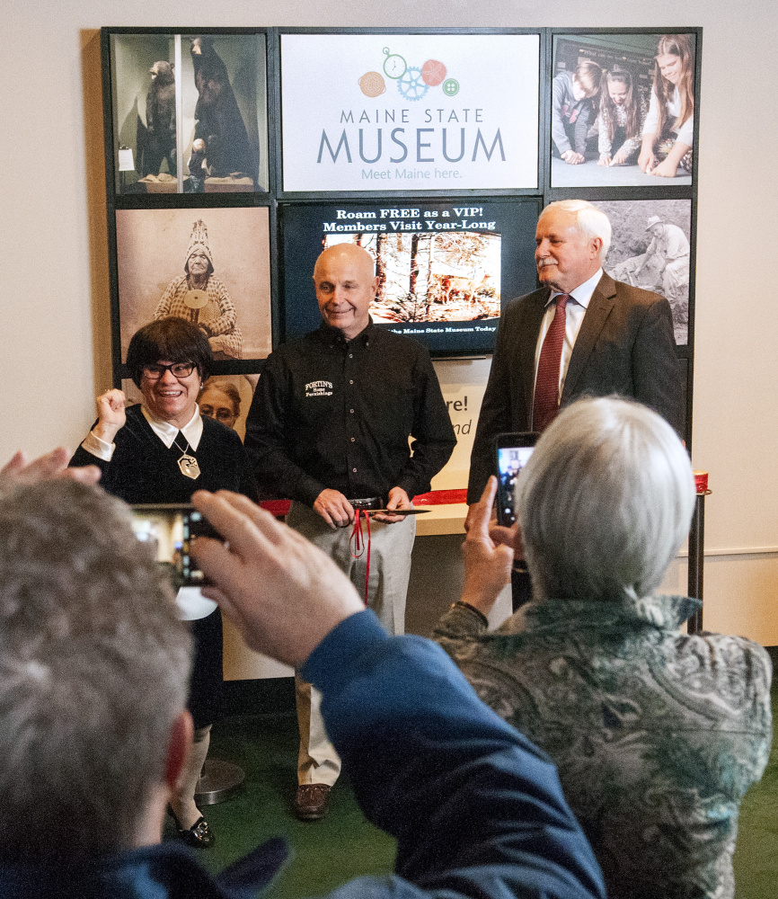 Jennifer Dube, development director of Friends of Maine State Museum, left; Mike Fortin, owner of Fortin's Home Furnishings; and Mike Reed, of FairPoint Communications, prepare to cut the ribbon on a new display Thursday at the Maine State Museum in Augusta.