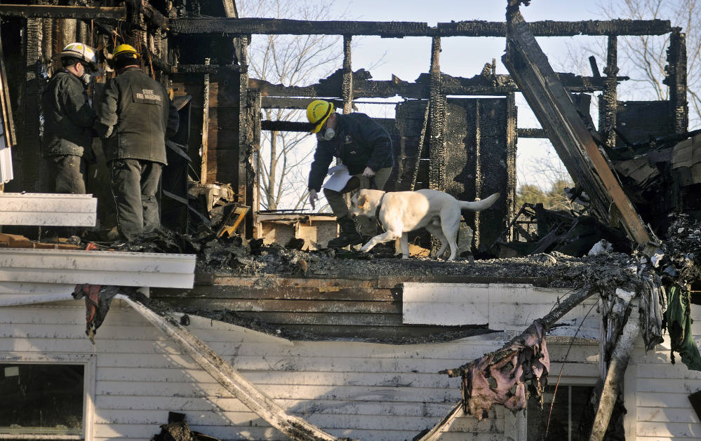 Investigators Chris Stanford, left, and Ed Archer of the Office of Maine State Fire Marshal observe their colleague Jeremy Damren handle his accelerant sniffing dog, Harry, while searching the burned remnants of a second floor apartment in a building in Richmond Sunday.