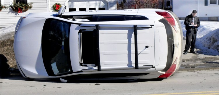 Victor Garay looks at a tablet Tuesday while waiting for a wrecker after the vehicle he was driving went off North Street in Waterville and rolled onto its side.