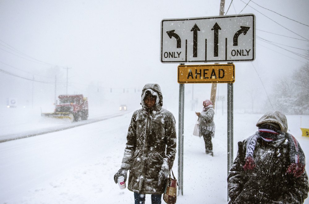 Charville Smith, left, Judy Simmons, center, and Cheryl Rosa stand at a Silver Lane bus stop, waiting for their ride home, after receiving a phone call from their employer, Cabela's, that it was closing due a snowstorm Thursday in East Hartford, Conn.