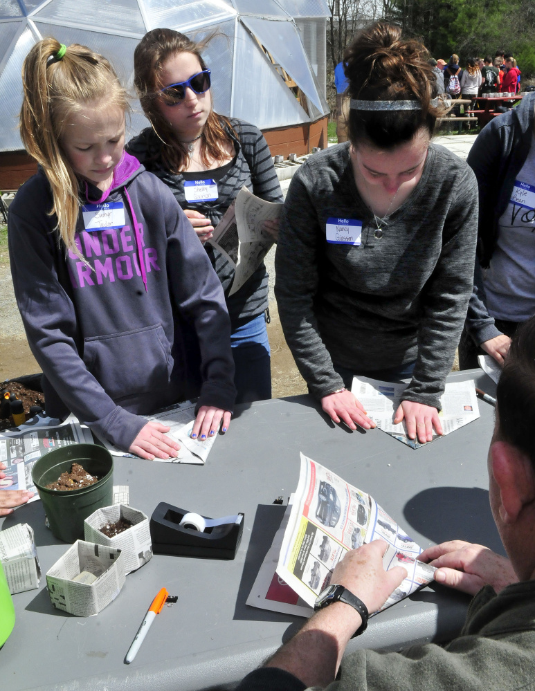 Skowhegan Middle School students Sumyr Taylor, left, Shelby Quirion and Nancy Giasson learn hold to fold newspaper into a biodegradable container to plant seedlings from instructor Gary Sinclair at one of the stations at the Marti Stevens Learning Center in Skowhegan during a forest field day on Wednesday.