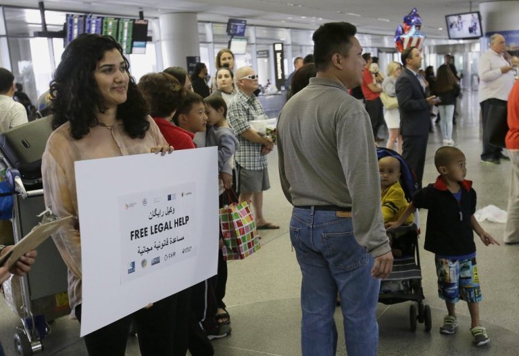 Sacha Maniar, program coordinator of the Asian Law Caucus, holds up a sign offering free legal help at the international terminal at San Francisco International Airport on Thursday. A scaled-back version of President Trump's travel ban took effect Thursday evening, stripped of provisions that brought protests and chaos at airports worldwide in January