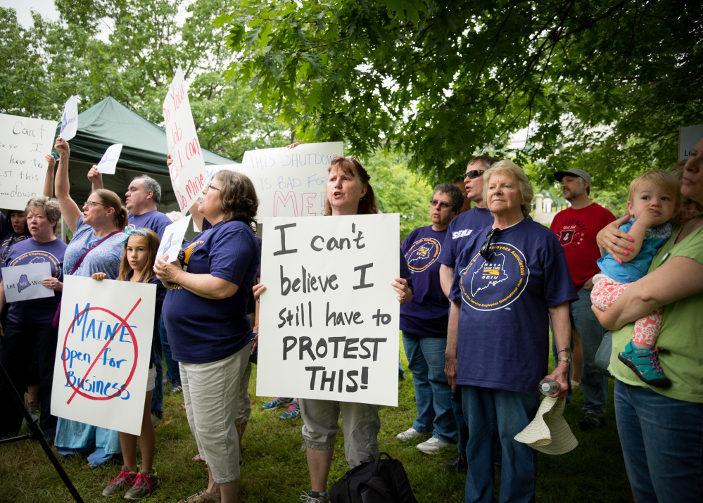 Robin Upton Sukefort, center, of Litchfield, holds a sign Saturday morning in Capitol Park in Augusta protesting the state government shutdown. She works for the state as a disability adjudicator and is out of work during the shutdown.