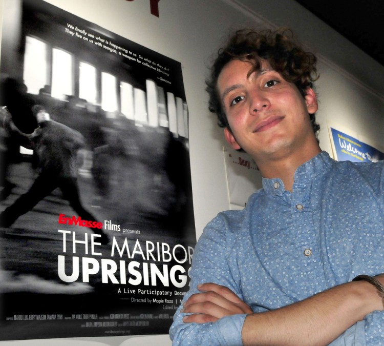 Milton Guillen, a former Colby student now employed by the college, stands beside a poster of the film "The Maribor Uprisings" on Wednesday inside Railroad Square Cinema in Waterville. Guillen co-directed the film, which is being screened at the Maine International Film Festival. Its next showing is scheduled for 9:30 p.m. Saturday at Railroad Square.