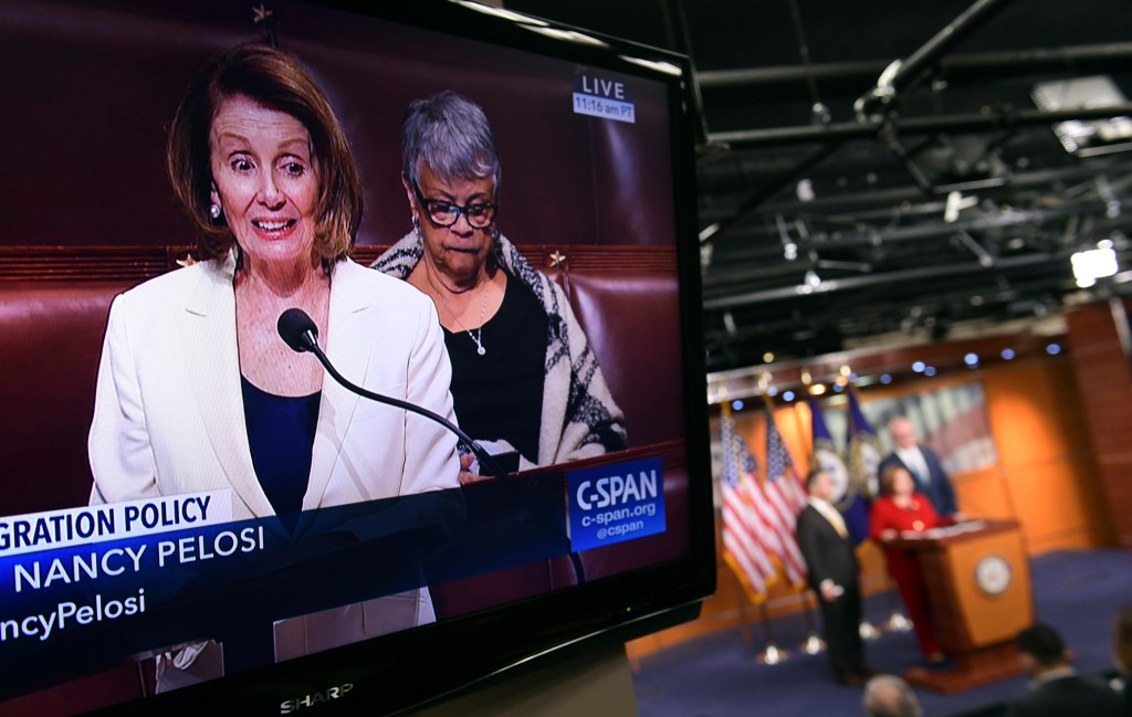 House Minority Leader Nancy Pelosi of Calif., is shown on television as she speaks from the House floor on Capitol Hill in Washington, Wednesday, Feb. 7, 2018, as a news conference that she was supposed to attend goes on in the background. 