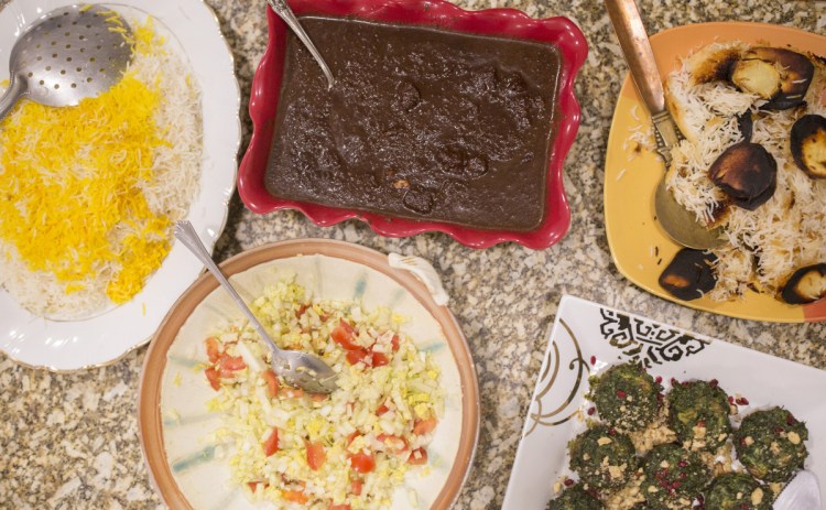 The Rohanis' meal celebrating Nowruz includes an herb-egg dish, kookoo sabzi, bottom right corner, and fesenjan, a chicken in pomegranate sauce dish, top center.