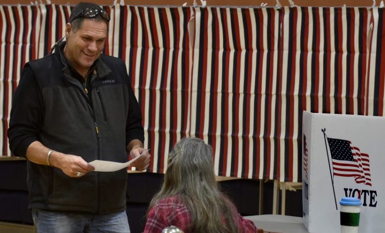 Norridgewock resident Brad Farrin speaks with election clerk Helen Balgooyen before casting his ballot during town elections at the Mill Stream Elementary School in Norridgewock on Monday.