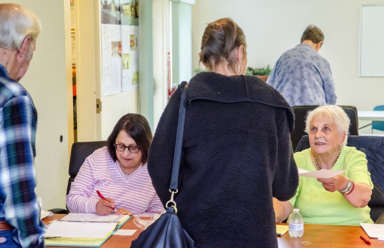 Ellie Emery, left, checks a voter's name off the list Tursday as Molly Wickwire hands a ballot to another voter during a referendum at the Randolph Town Office. Randolph residents were voting on whether to close T.C. Hamlin School.