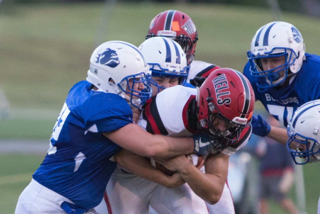 Madison defenders Brad Peters, left, and Jacob Meader tackle Wells ballcarrier Tyler Bridge during a season-opening game Friday night at Madison.