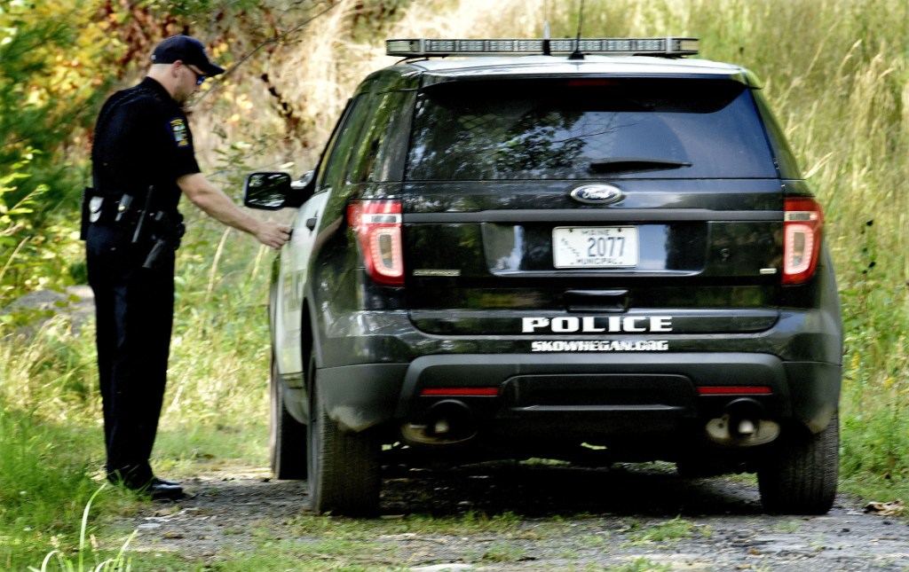 Skowhegan police officer Alex Burns returns to his cruiser after searching on foot the shore of the Kennebec River near the eddy in Skowhegan for the driver of a vehicle that crashed off Water Street early Sunday morning. Police say the man then jumped out of the vehicle and climbed down a steep embankment at the rivers edge off Water Street.