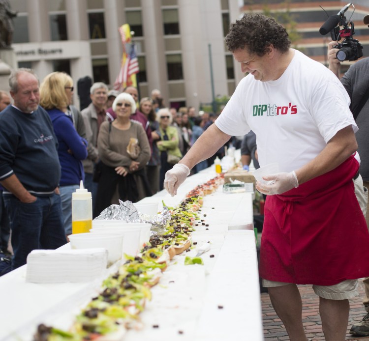 Sam Di Pietro, owner of Di Pietro's in South Portland, puts the finishing touches on his section of the huge Italian sandwich built on Monument Square in Portland on Thursday.