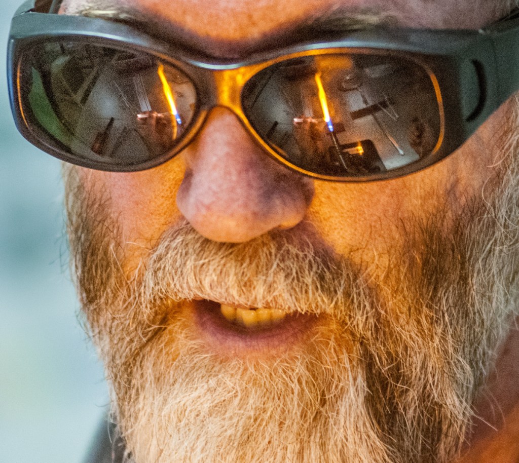 The torch used to heat glass is reflected in James Byrnes' glasses as he teaches a class on Saturday at Stained Glass Express in Manchester.